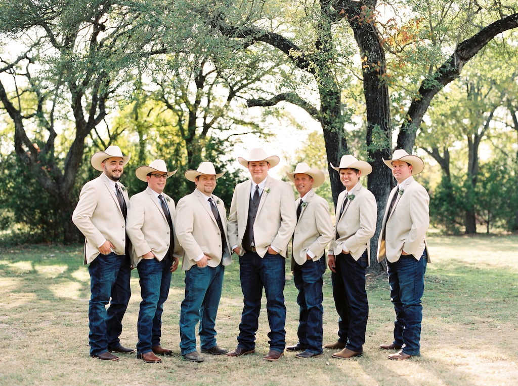 Groom and six groomsmen wearing cowboy hats pose together before the wedding reception at Kindred Oaks in Georgetown, Texas.