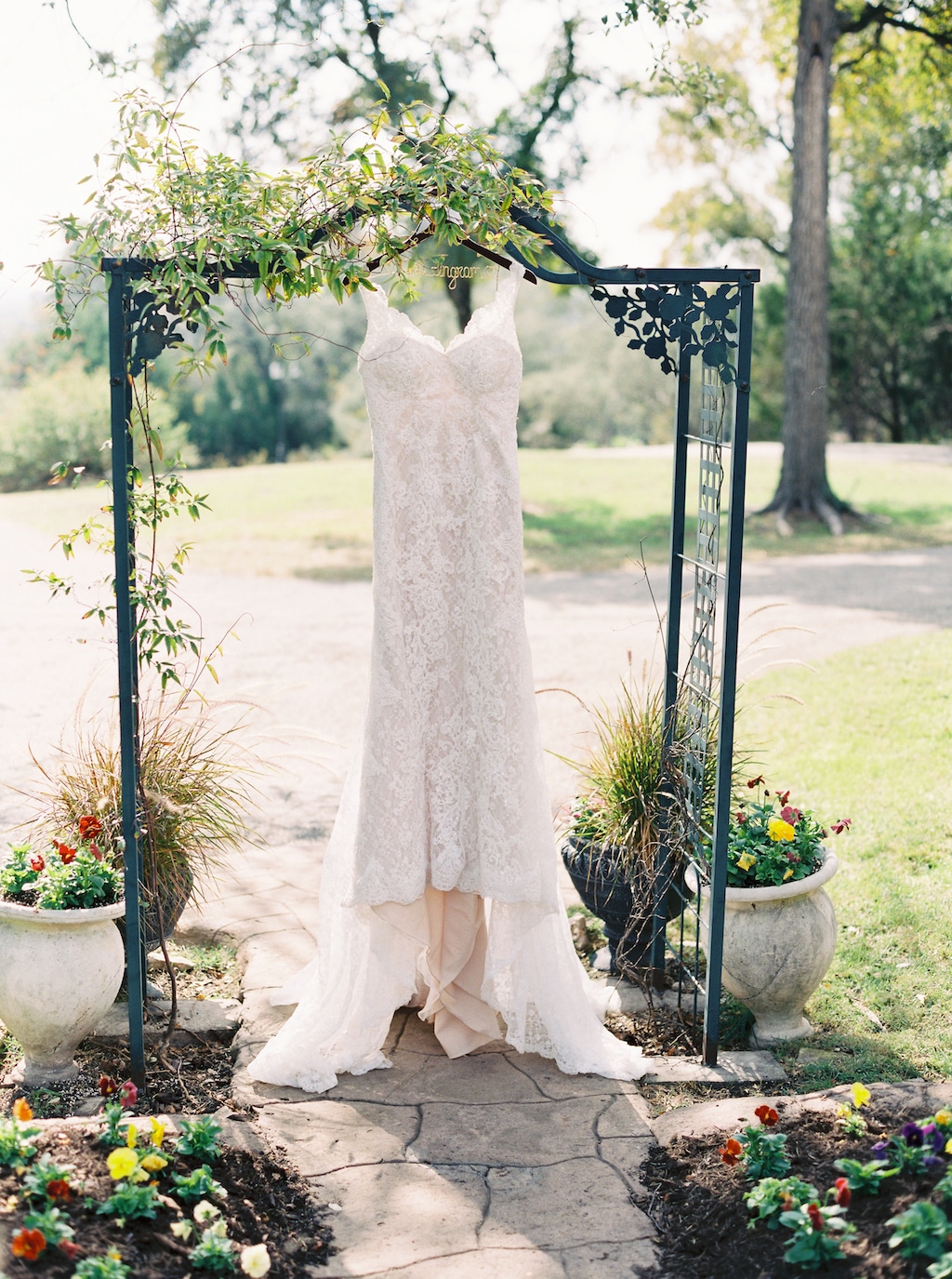 A lacy wedding dress hangs from a small green arbor on the grounds of a wedding venue in Georgetown, Texas.