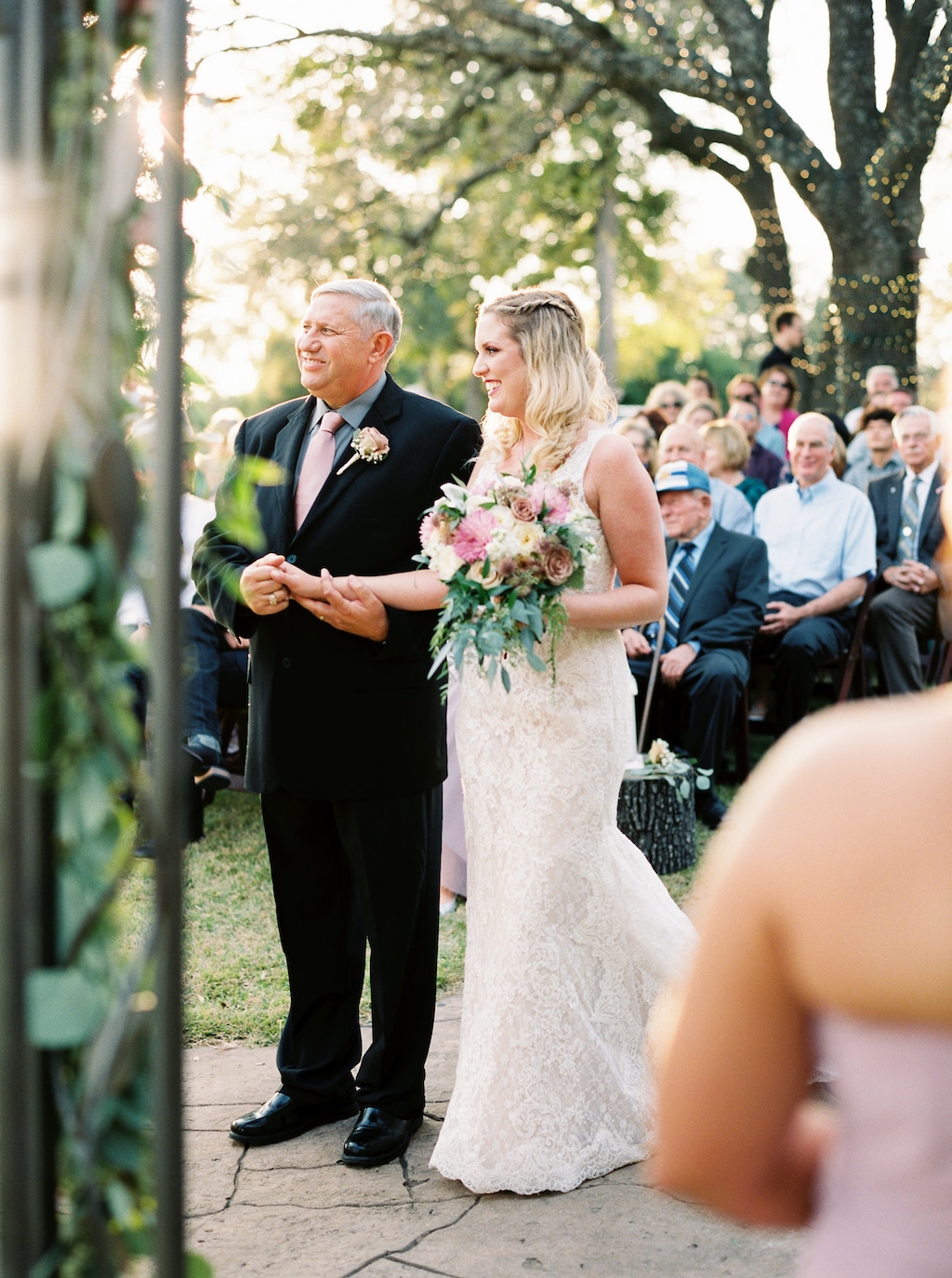 A smiling bride and her father stand at a Georgetown, Texas wedding ceremony while guests look on from behind.