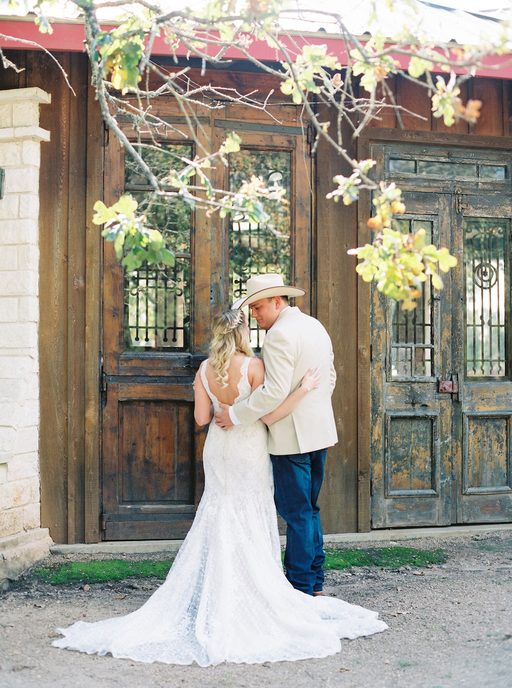 A bride and groom, with their backs to the camera, hug each other next to pairs of weathered doors outside at a Georgetown, Texas wedding venue.