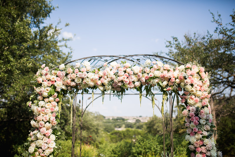 An outdoor wedding arbor in Georgetown, Texas is covered in soft colored florals and greenery.