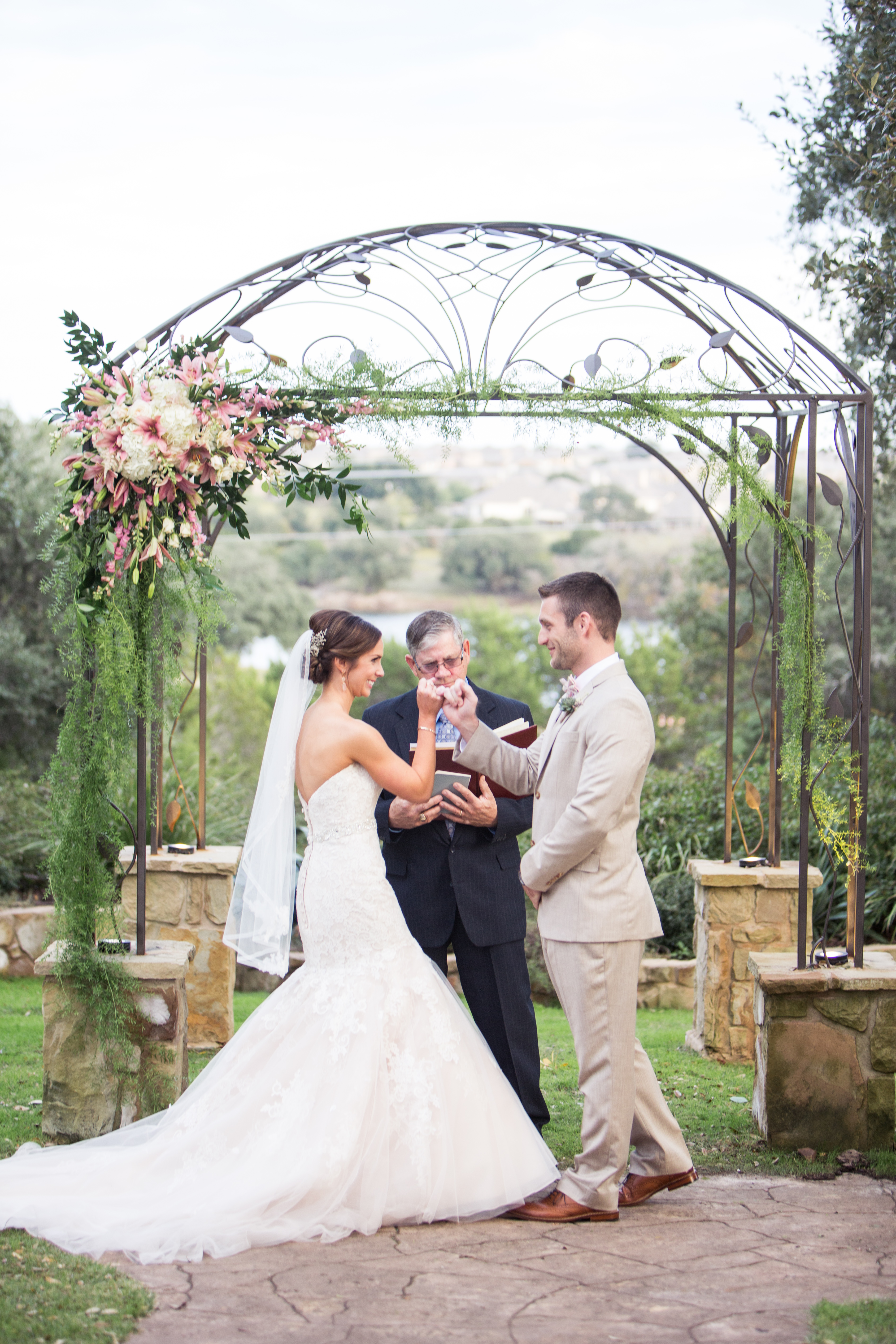 A bride and groom lock pinky fingers under a beautifully decorated arbor at Kindred Oaks in Georgetown, Texas. Photo by Shelley Elena Photography.