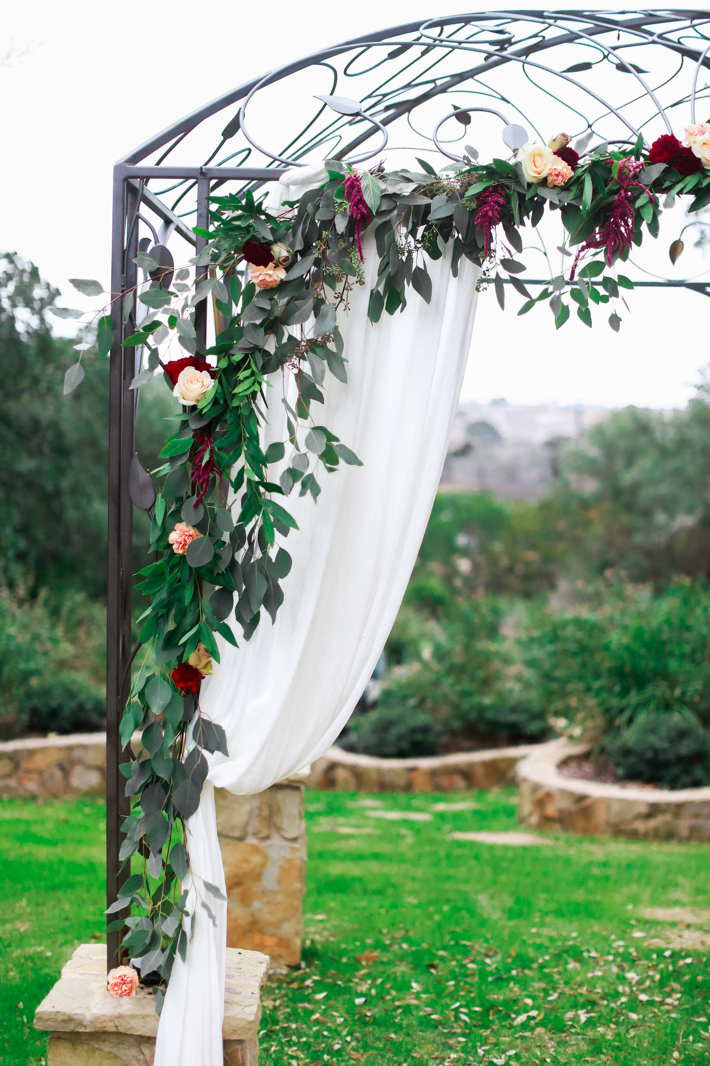 An iron arbor is decorated with white cloth and greenery at a wedding venue in Georgetown, Texas. Photo by Jeff Brummett Visuals.