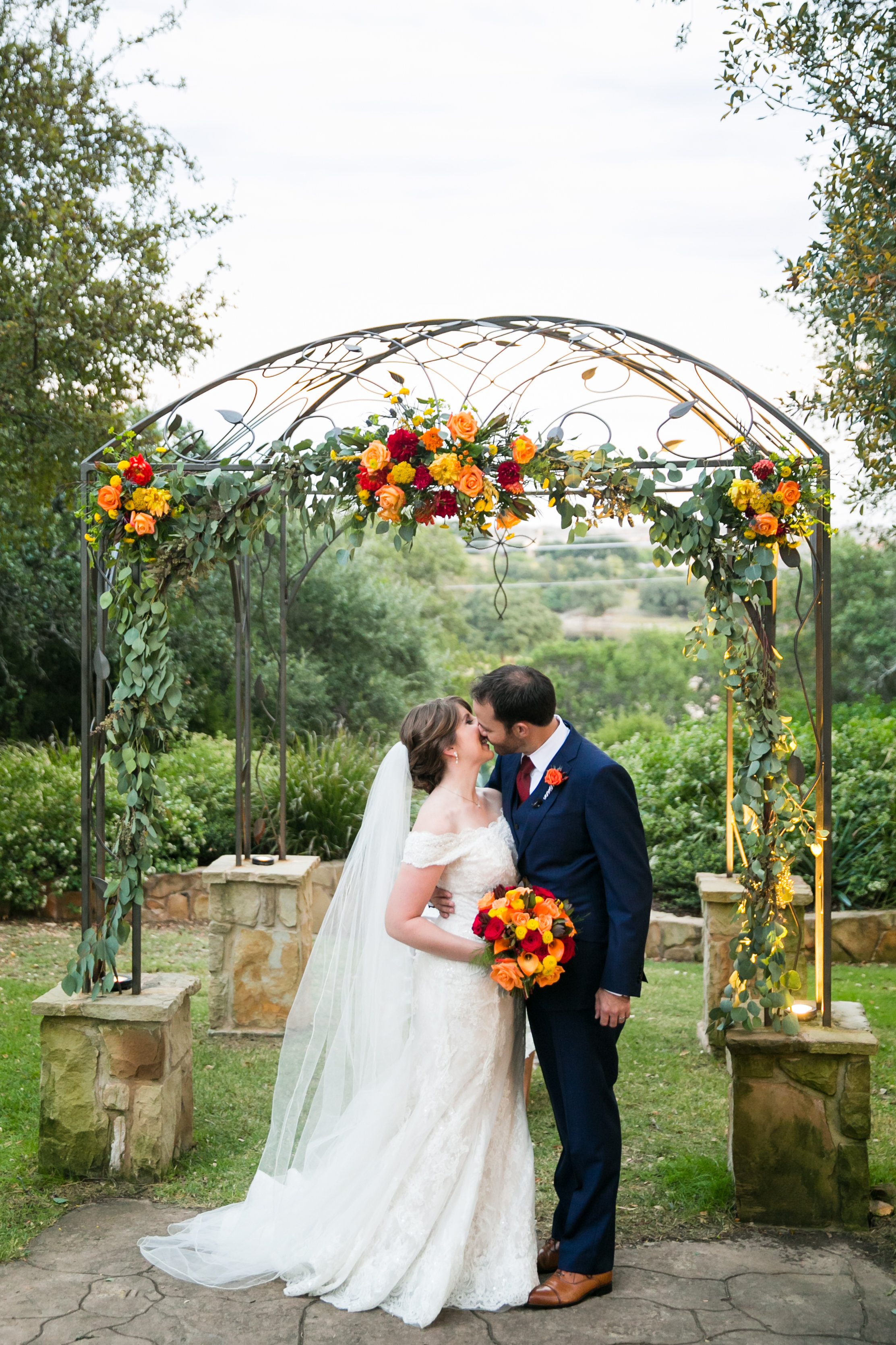 Fall outdoor wedding ceremony at Kindred Oaks in Georgetown, Texas. A bride and groom kiss underneath their wedding ceremony arbor at a Georgetown, Texas wedding venue. Photo by Tank Goodness Photography.