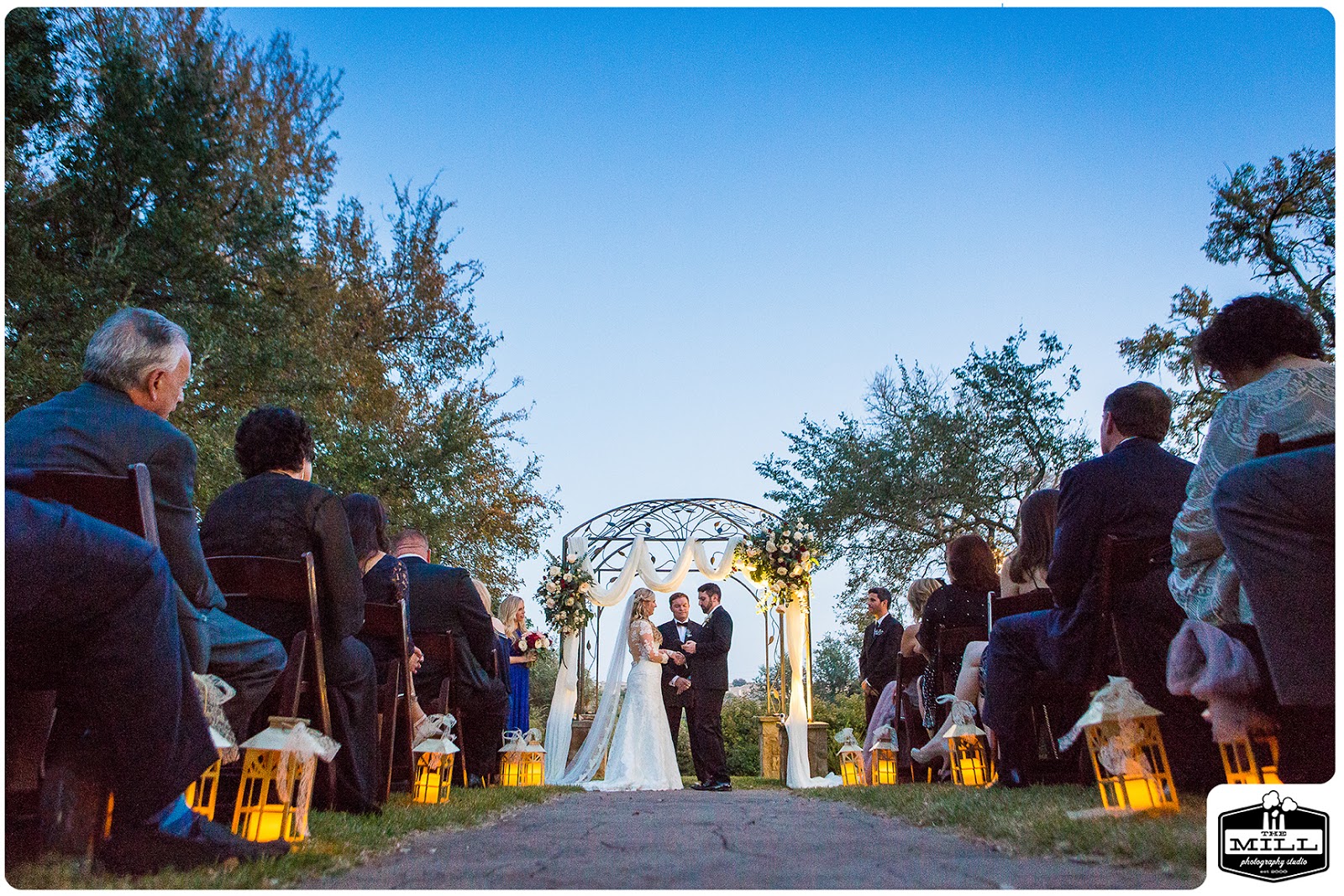 A bride and groom stand under an arbor at the end of a lighted aisle at their evening wedding in Georgetown, Texas. Photo by The Mill Photography Studio.