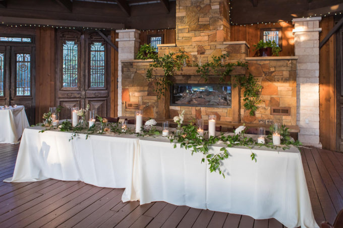 A long head table is decorated in greenery by ZuZu